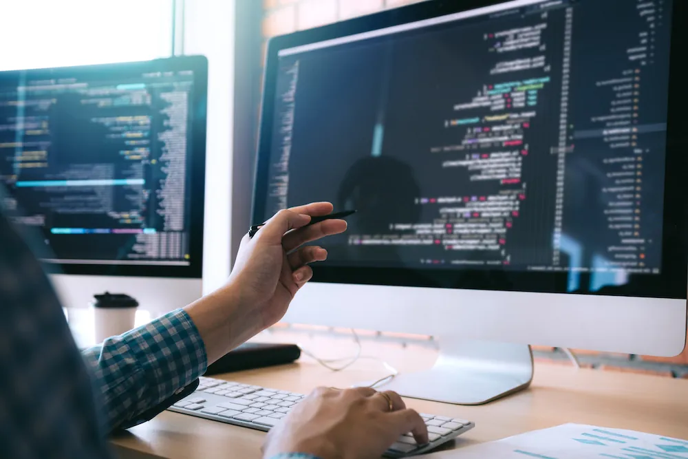 Software developer holds the pen pointing to the computer screen and is analyzing the code.